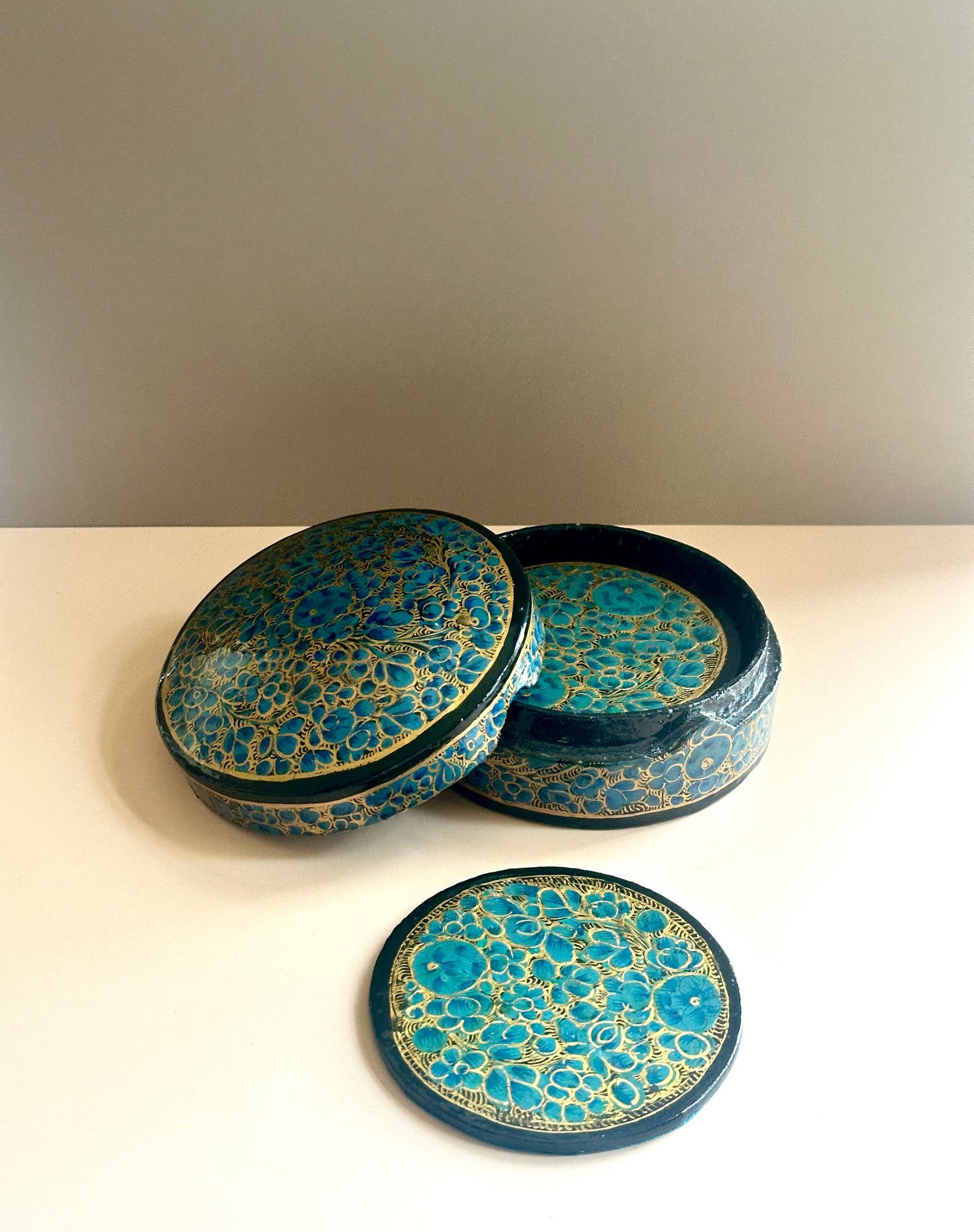a box of handmade and hand-painted teal blue Kashmiri coasters in a floral design