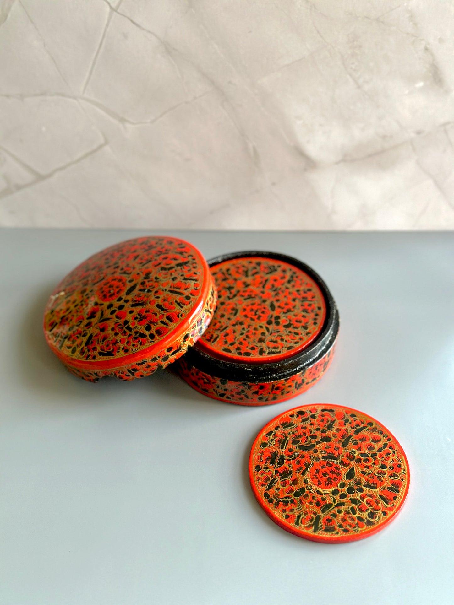 a box of handmade and hand-painted red and gold Kashmiri coasters in a floral design