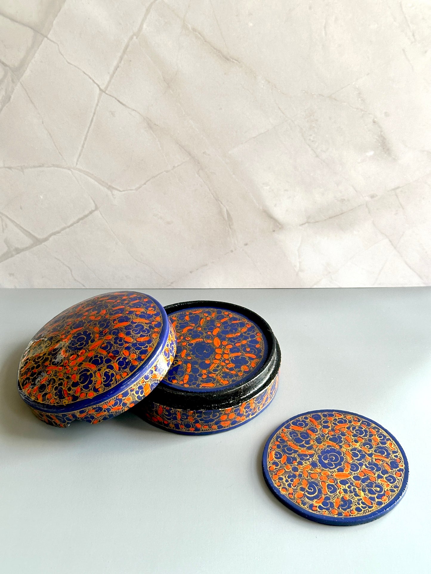 a box of handmade and hand-painted indigo and orange Kashmiri coasters in a floral design