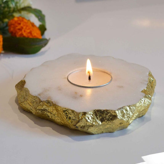a stunning handmade marble candle holder with golden foiling on edges containing a lit tea light candle