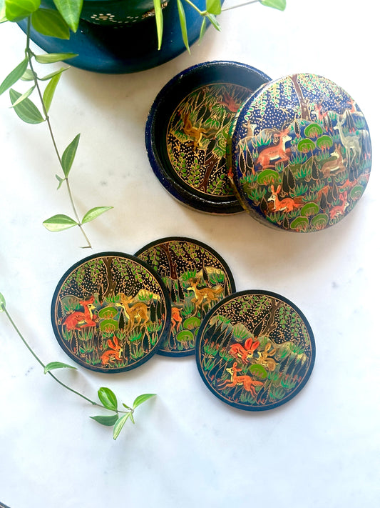 a set of beautiful artisanal hand-painted blue and gold coasters with jungle motifs kept on a table with a plant