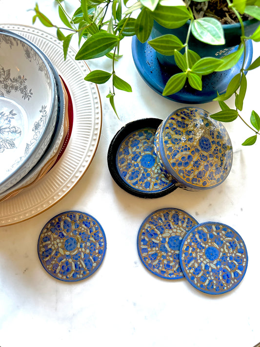 a set of beautiful artisanal hand-painted blue and gold coasters kept on a table with a plant and some dinnerware