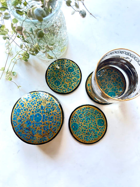  a set of beautiful artisanal hand-painted teal blue and gold coasters kept on a table with a plant