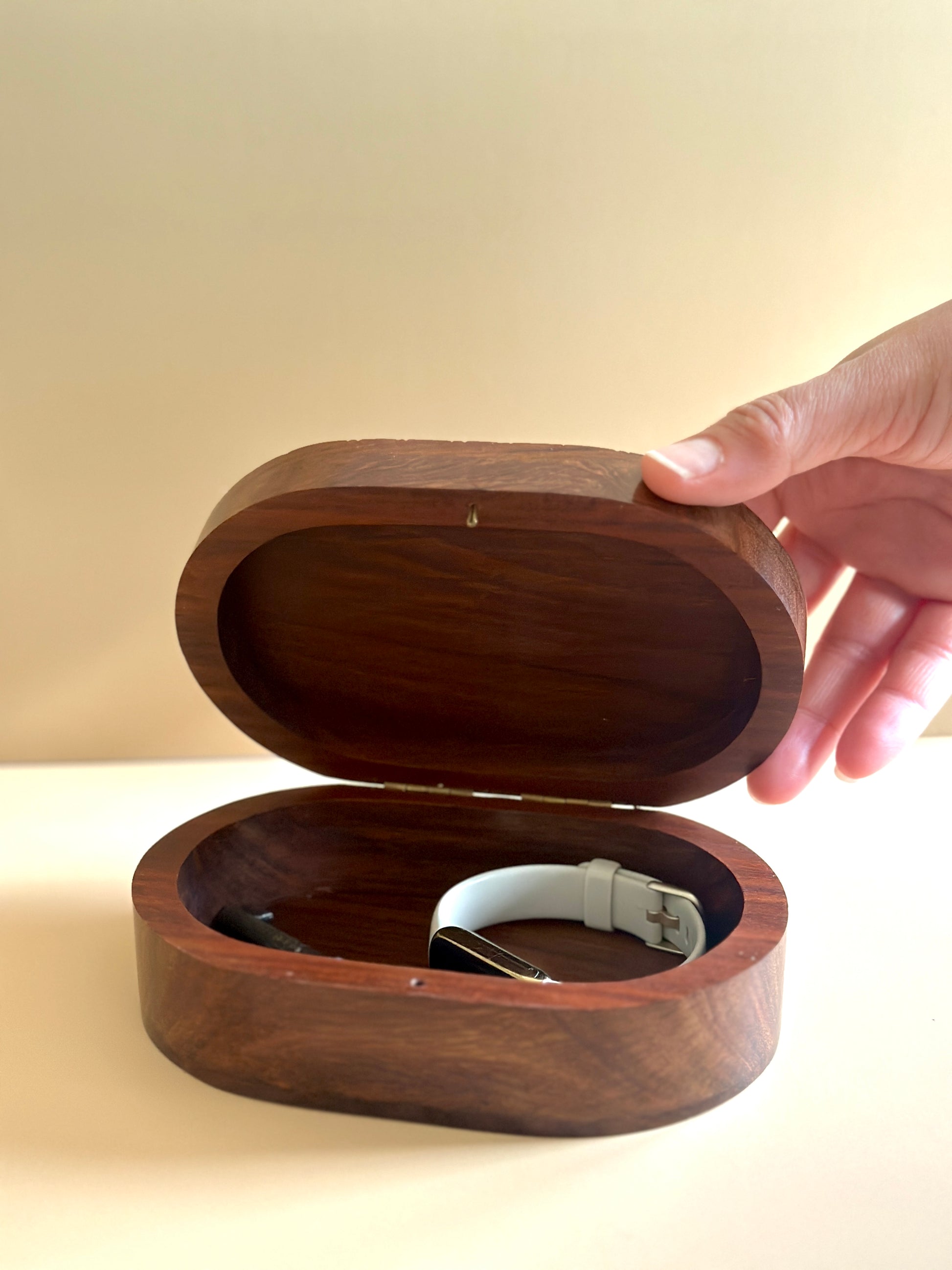 a hand holding open an oval shaped wooden trinket box with things inside