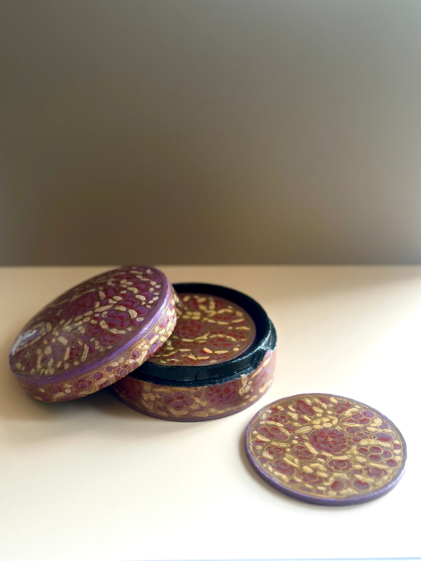 a box of handmade and hand-painted pink Kashmiri coasters in a floral design