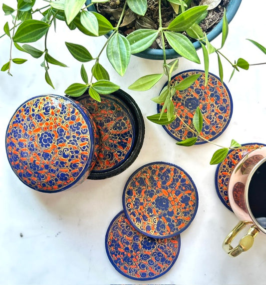 a set of beautiful artisanal hand-painted indigo and orange coasters with a floral design kept on a table with a plant
